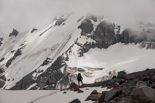 Человек с походным снаряжением стоит на скале вокруг остатков снега — стоковое фото