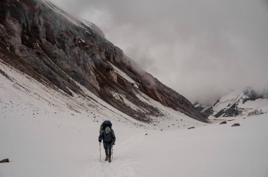 Dağdaki tepeye tırmanan bir adam yürüyüş sopaları ve sırt çantasıyla