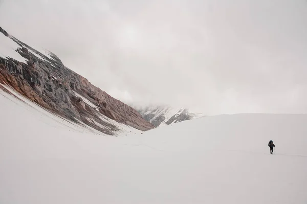 Ο άνθρωπος σκαρφαλώνει στο χιόνι στο βουνό με μπαστούνια πεζοπορίας και σακίδιο πλάτης — Φωτογραφία Αρχείου