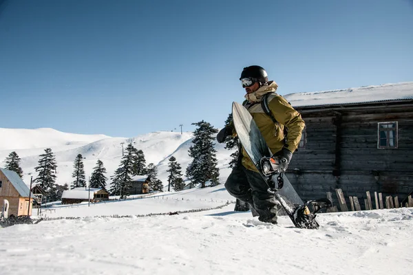 Freerider macho caminando por la ladera nevada de la montaña con una tabla de snowboard —  Fotos de Stock