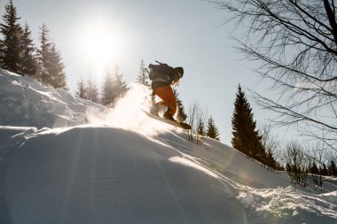 Serin bir insan, parlak güneşe karşı bir snowboardla dağdan atlar.