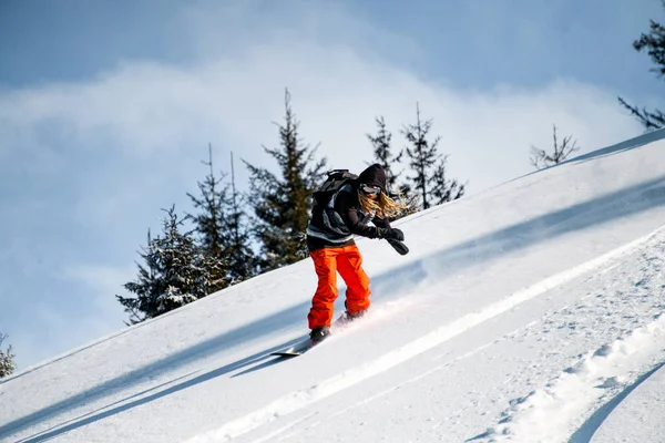 Pessoa com dreadlocks e em calças vermelhas desliza para baixo da montanha em um snowboard — Fotografia de Stock