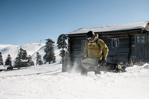 El hombre camina con una tabla de snowboard negra en sus manos sobre el fondo de las casas — Foto de Stock