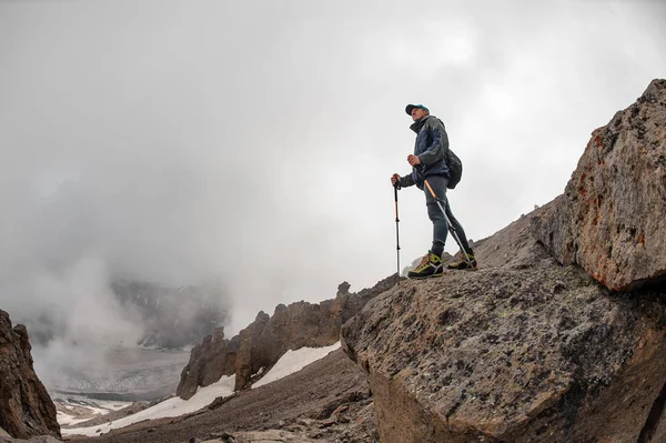 Uomo in piedi sulla sporgenza di pietra guardando sulla nebbia bianca — Foto Stock