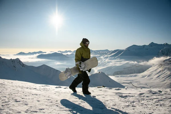 Kerel met snowboard wandelingen op zonnige bergtop — Stockfoto