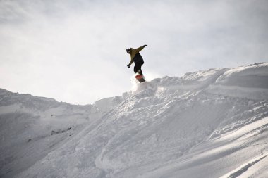Freerider in anorak jumping on a snowboard in mountains