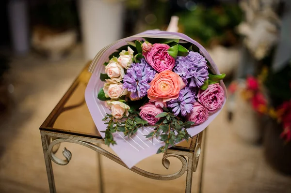 กองดอกไม้ต่าง ๆ ในกระดาษสีม่วงวางบนเก้าอี้ — ภาพถ่ายสต็อก