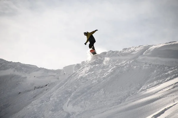 Freerider em anorak pulando em um snowboard em montanhas — Fotografia de Stock