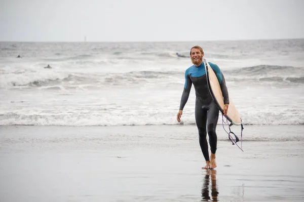 Man with surfboard walks in front of sea — Stock Fotó
