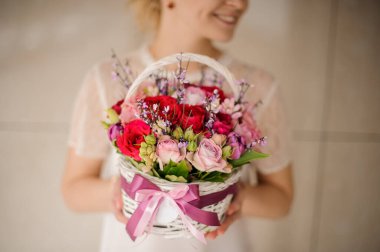 Girl holding a spring basket of pink and red roses with green leaves and pink branches