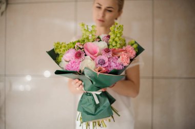 Girl holding a spring bouquet of tender green, white and pink flowers wrapped in a dark paper