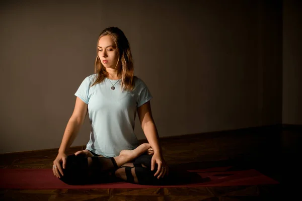 Woman in sport clothes practicing yoga in a studio room sitting in lotus pose — Stock fotografie