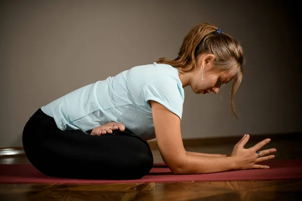 Girl in sport clothes practicing yoga in a studio room in the lotus pose hold elbows on the floor — Stockfoto