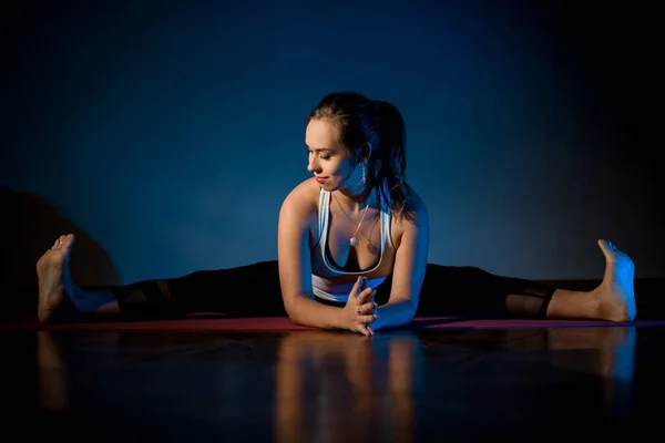 Girl in sport clothes practicing yoga in a studio room in the stretching pose on the floor — Stock fotografie