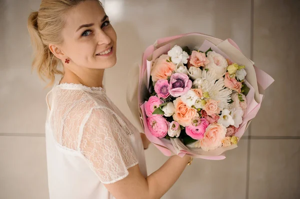 Menina segurando um buquê de primavera de cor macia flores diferentes com folhas em um papel rosa — Fotografia de Stock