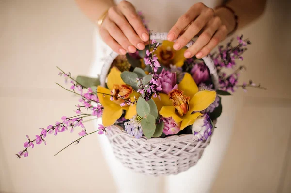 Girl holding a spring basket of tender color yellow orchids with green leaves and pink branches — Stockfoto