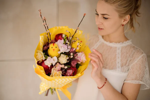 Menina segurando um buquê de primavera de flores diferentes decoradas com ramos de salgueiro, pequeno brinquedo chiken envolto em papel amarelo — Fotografia de Stock