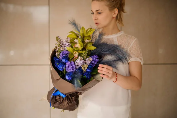 Menina segurando uma composição de buquê de flores de primavera escura com flores, penas azuis em um papel dourado — Fotografia de Stock