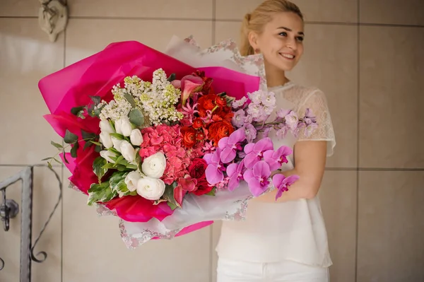 Smiling girl holding a huge spring bouquet of different white, red, pink and rose color flowers wrapped in paper — Stock Photo, Image