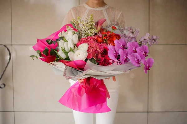 Девушка держит огромный весенний букет из различных белых, красных, розовых и розовых цветов, завернутых в бумагу — стоковое фото