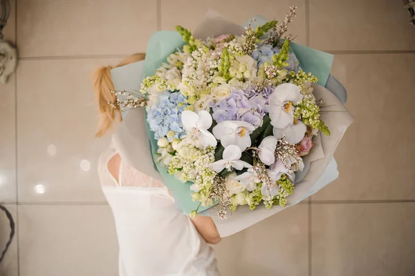 Fille tenant un énorme bouquet de printemps de différentes fleurs blanches, vertes et tendres de couleur violette enveloppées dans du papier — Photo