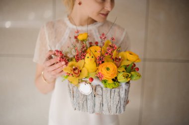 Shy girl holding a composition in a wood trunk piece with yellow flowers, branches and toy chicken