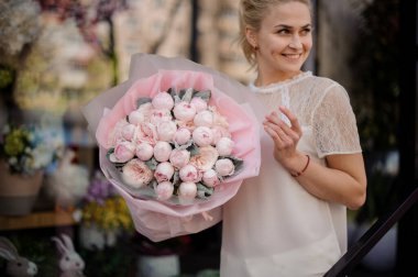 Girl holding a spring bouquet of tender rose color peonies wrapped in a pink paper