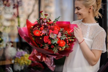 Girl holding a spring bouquet of different red color flowers decorated with branches