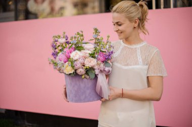 Girl holding a violet color velvet box of tender pink, creamy and white flowers decorated with a green branches
