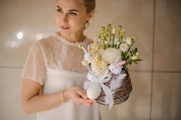 Donna che tiene una composizione in una pentola decorata con spago con boccioli di fiori, piume bianche e conigli — Foto Stock