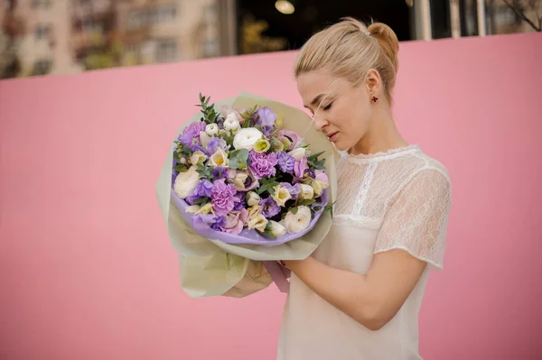 Girl holding a spring bouquet of tender violet and white color different flowers with leaves in a purple paper — Stockfoto