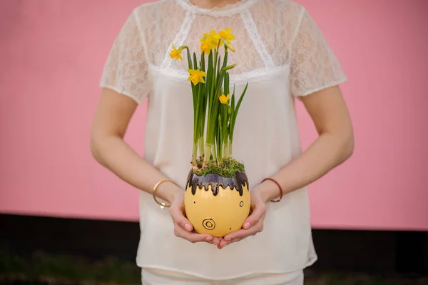 Niña sosteniendo una flor en forma de olla de chocolate con el narciso amarillo con hojas verdes — Foto de Stock