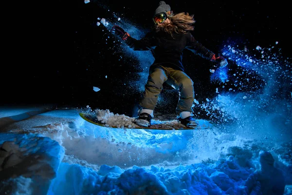 Female snowboarder doing stunts on blue light background — Stockfoto