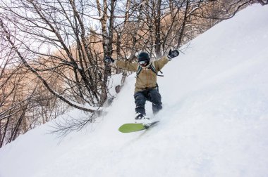 Active male snowboarder dressed in a grey brown sportswear riding down the sountain slope
