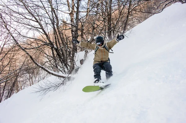 Active male snowboarder dressed in a grey brown sportswear riding down the sountain slope — 图库照片