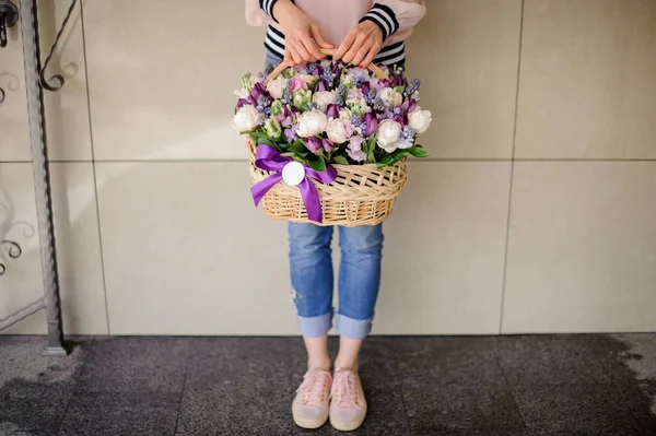 Молодая женщина держит композицию с различными цветами в декоративной корзине в руках . — стоковое фото