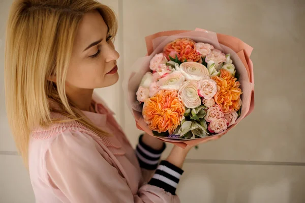 Young woman holding a beautiful flower bouquet and looks at it — 图库照片