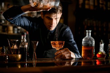 Barman pours a cocktail from one glass to other wineglass.