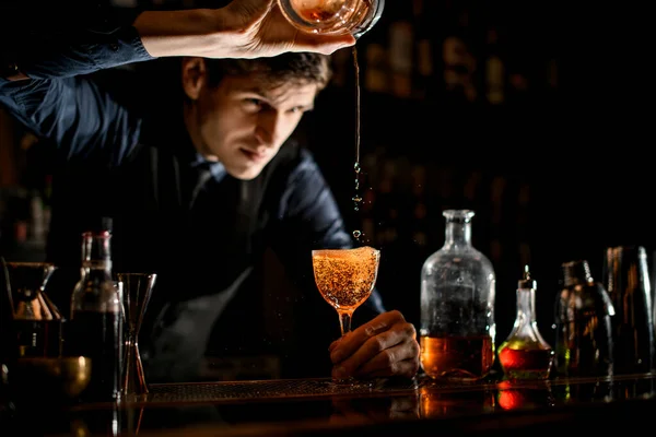 Barman holds wineglass in his hand while pouring a cocktail into it. — Stockfoto