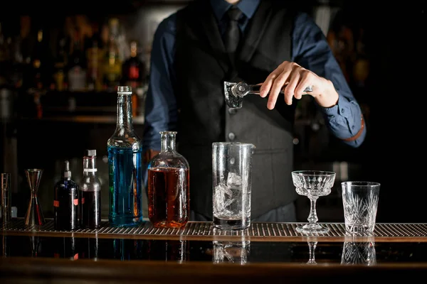 Bartender is preparing alcoholic cocktail with ice in a glass behind the bar. — Stock fotografie
