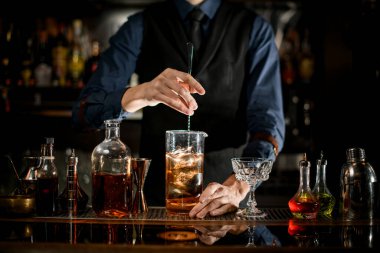 Bartender mix cold alcoholic cocktail with ice by spoon.