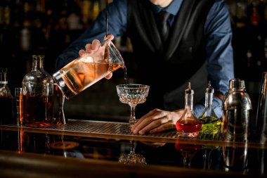 Bartender holding glass of cold cocktail and pours it into wineglass.