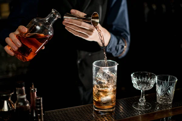Barman measures the ingredients for cocktail from bottle with brown alcohol drink. — Stockfoto