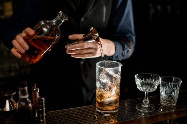Bartender professionally add necessary ingredient to glass with cocktail.