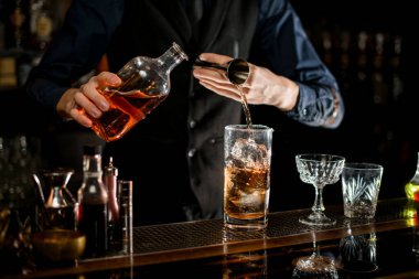 Bartender in blue shirt add necessary ingredient to glass with cocktail.