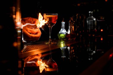 close-up bartenders hands which sets fire near cocktail glass.