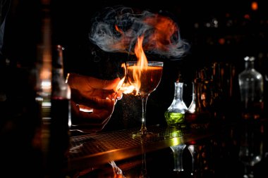 close-up bartenders hands which sets fire near cocktail wineglass.