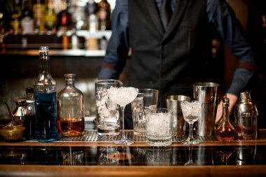 bar counter with a variety of glasses with ice and several bottles with alcoholic drinks