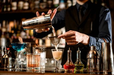 Barmen kadehten bardağa kokteyli nazikçe doldurur..