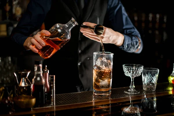 Bartender in blue shirt add necessary ingredient to glass with cocktail. — Stockfoto